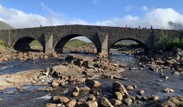 Stone bridge over a river with people crossing, surrounded by a rocky landscape.