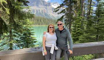 Couple posing by a turquoise lake surrounded by mountains.