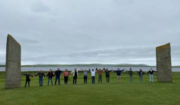 Group holding hands in a circle between two large standing stones.