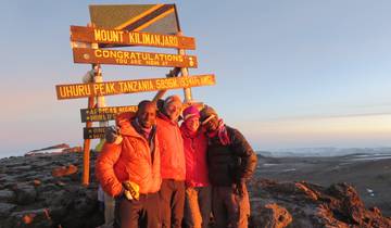 Group posing at the summit of Mount Kilimanjaro with summit signs.