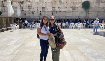 Two women smiling in front of the Western Wall in Jerusalem.