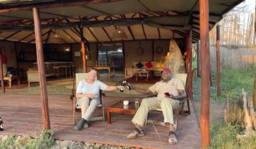 Two people enjoying drinks on a veranda overlooking nature.