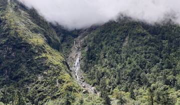 A scenic view of a mist-covered waterfall in a lush mountain landscape.