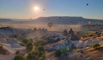Hot air balloons float over Cappadocia's unique landscape at sunrise.