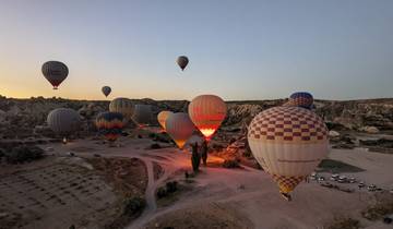 Hot air balloons rising at sunrise over rock formations.