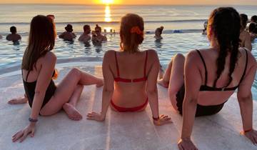 Three women sitting poolside watching the sunset over the ocean.