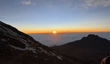 Sunrise over a mountainous landscape with clouds below.