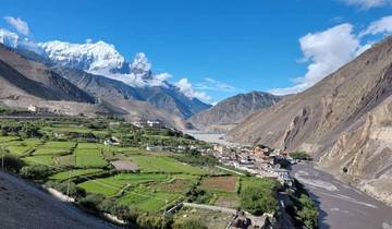 A village situated in a lush green valley with snow-capped mountains.