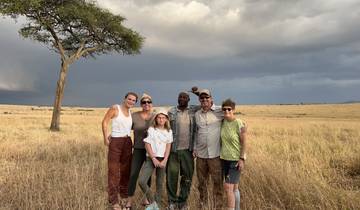Group of people posing on a savanna with a tree under a cloudy sky.