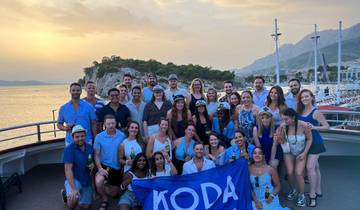 A large group of people holding a flag on a boat during sunset.