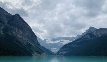 Lake surrounded by rugged mountains and cloudy sky.