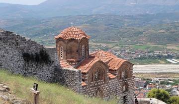 Historic Orthodox church with a scenic backdrop of mountains and a town.