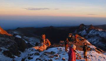 People on a snowy mountain peak at sunrise.