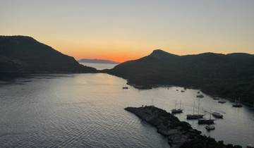 Sunset over a serene bay with yachts and hills.