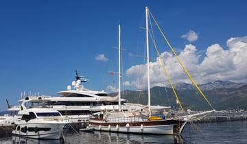 Yachts moored at a marina with mountains in the background.