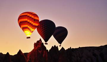 Hot air balloons above rock formations at sunset in Cappadocia.