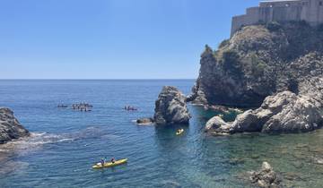 People kayaking near rocky cliffs by the sea.