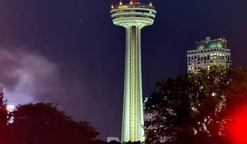 Skylon Tower illuminated at night, surrounded by trees and lights.