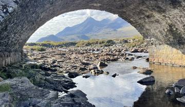 Stunning mountain view framed under a stone arch bridge.