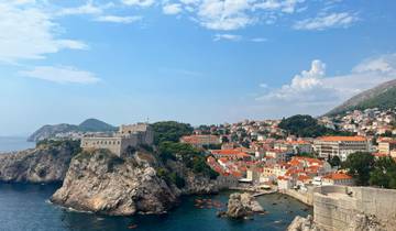 A scenic view of Dubrovnik with medieval walls and orange rooftops along the coastline.