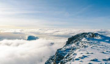 Snow-capped mountain peak surrounded by clouds and a clear blue sky.