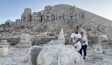 Two people posing in front of large ancient stone heads on a mountain.