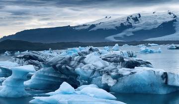 Icebergs floating on a serene glacial lagoon with mountains in the background.