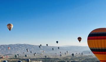 Multiple hot air balloons in the sky over a valley.