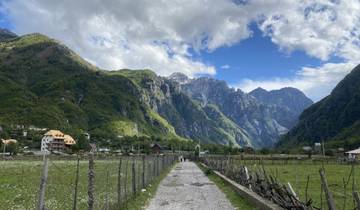 Mountain valley view with a path leading towards the mountains and houses along the way.