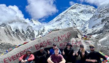 Group of people posing at Everest Base Camp with snowy peaks.