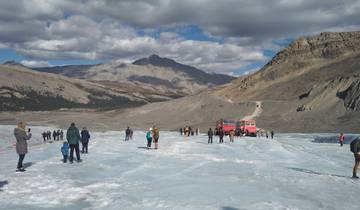 Tourists walking on a glacier with mountains in the background.