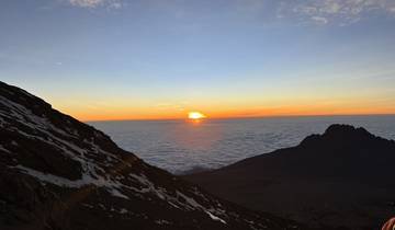 A beautiful sunrise seen from a high mountain, with clouds below and a distant peak.