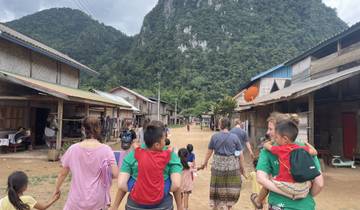 Group of people walking through a rural village with mountains in the background.