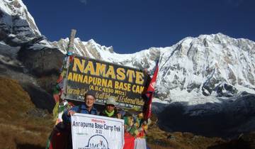 People at Annapurna Base Camp with sign and snowy mountains.