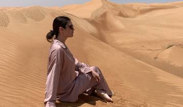 Person sitting on sand dunes in a desert.
