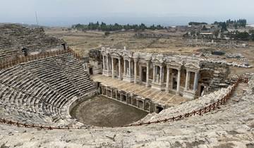 An ancient amphitheater ruin with stone seats and a large stage in a dry landscape.