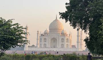 The Taj Mahal behind trees with people in the foreground.