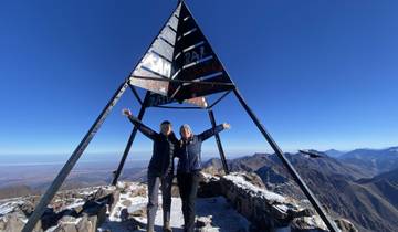 Two people at the peak of a mountain next to a metal structure.