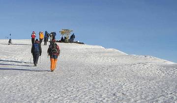 Group of hikers walking on a snow-covered path with summit sign.