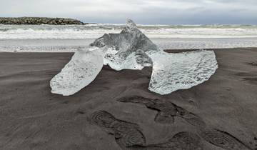 Ice on black sand beach with ocean waves in the background.