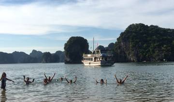 People swimming near a boat with limestone karsts in the background.