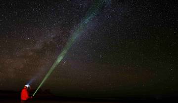 Person with a green laser pointer under a starry sky.