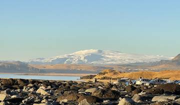 A distant glacier with rocky shore and vehicles.