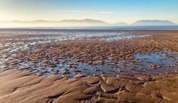 Wide sandy beach with water and distant mountains.