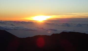 Sunrise view above the clouds with a silhouette of a mountain.