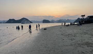 Beach scene at sunset with people and a cruise ship.