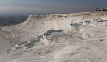 Pamukkale's travertine terraces filled with water under a hazy sky.