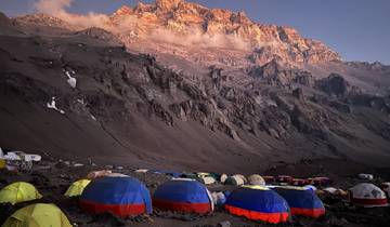 Mountain campsite with colorful tents and a rocky peak at sunrise.