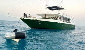 Large boat anchored on the sea with small dinghy nearby.