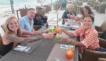 A group of people raising glasses at an outdoor dining setting by the beach.